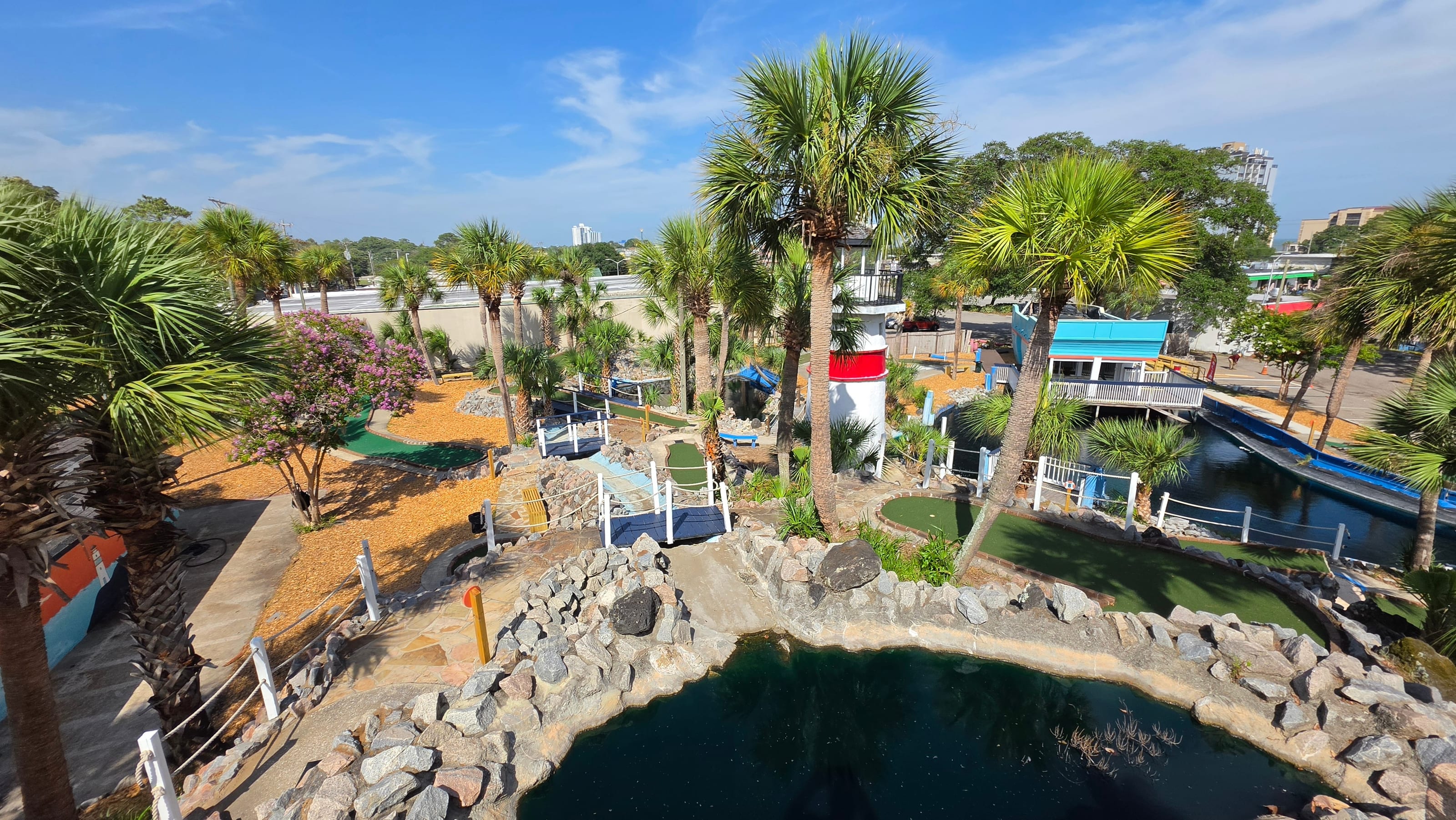 Elevated view of Captain Myrtle Mini Golf with a lighthouse, palm trees, and water features
