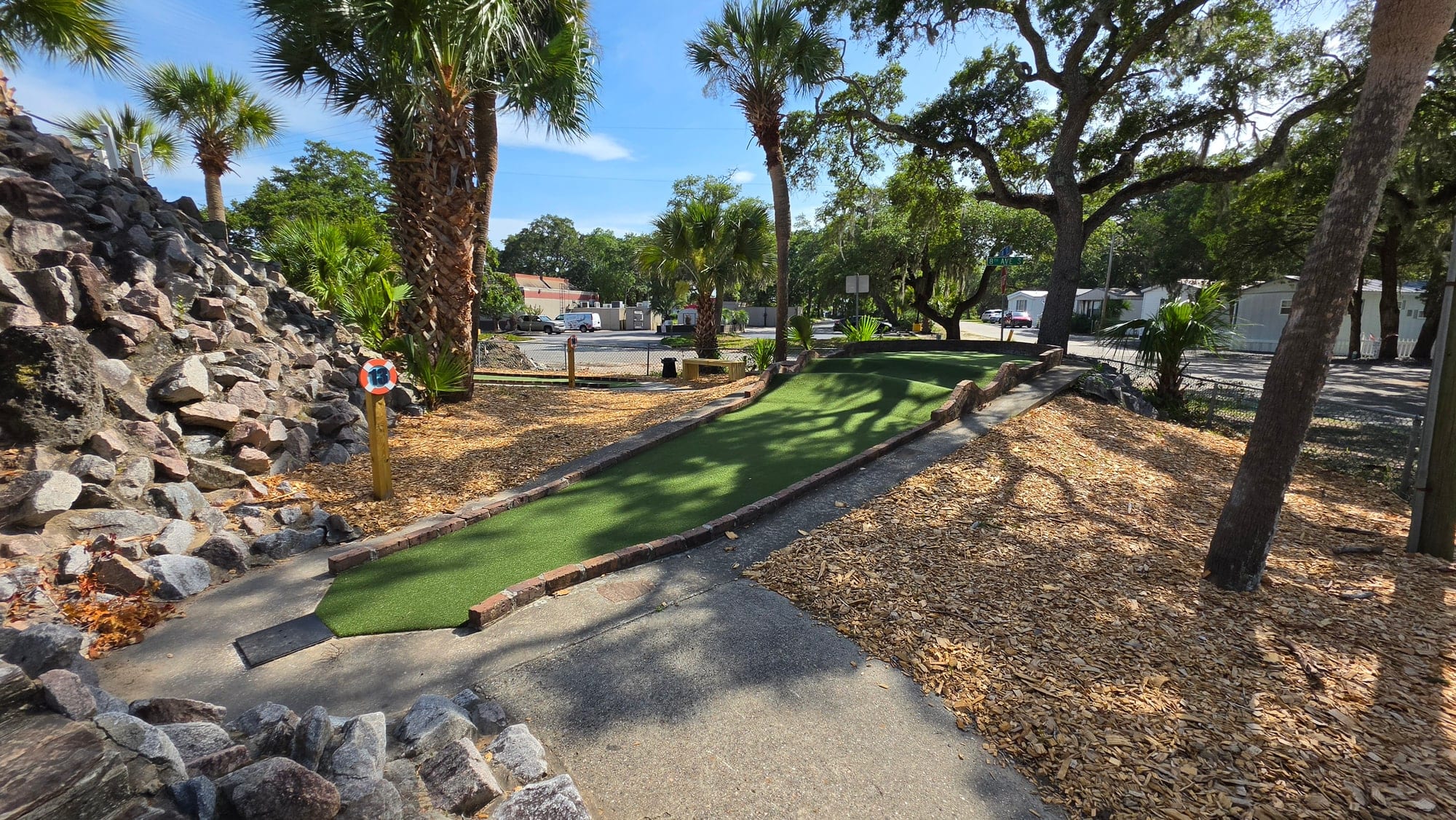 Hole 13 putting green beneath oak and palm trees at Captain Myrtle Mini Golf